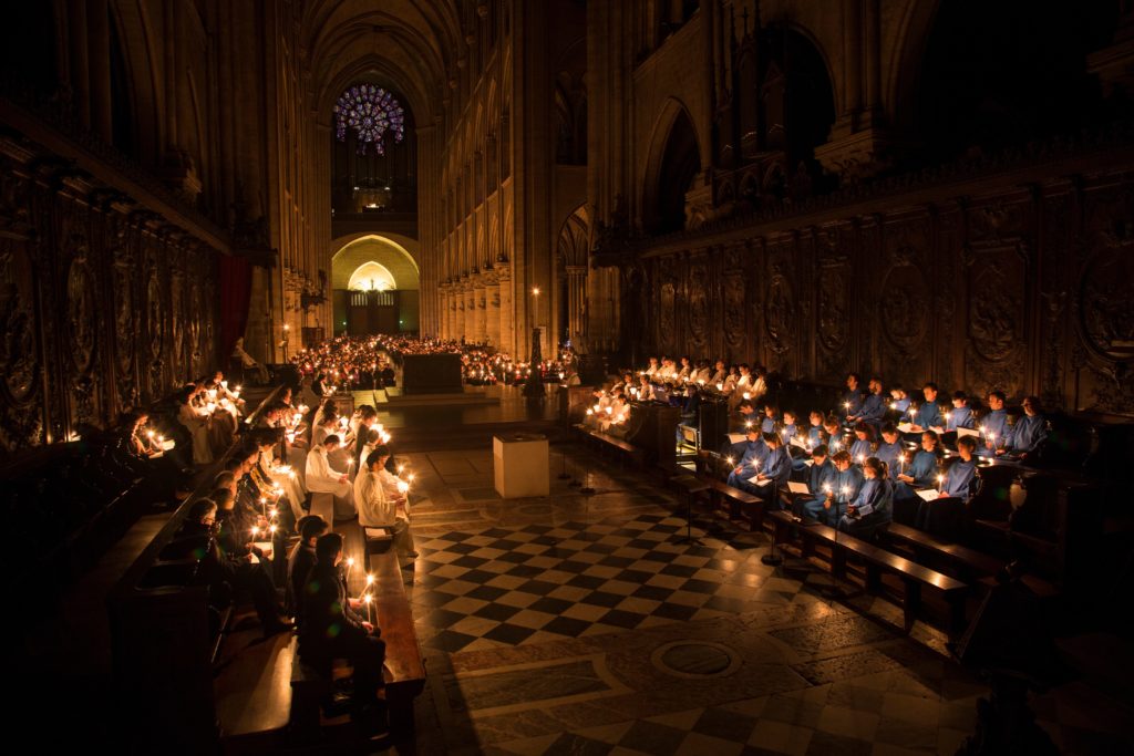 Mit Kerzenlicht in der Hand sitzen die Domchöre von Notre-Dame im Hochaltar. Ein Jahr nach der Notre-Dame-Katastrophe ist die Kathedrale immer noch eine ungesicherte Baustelle